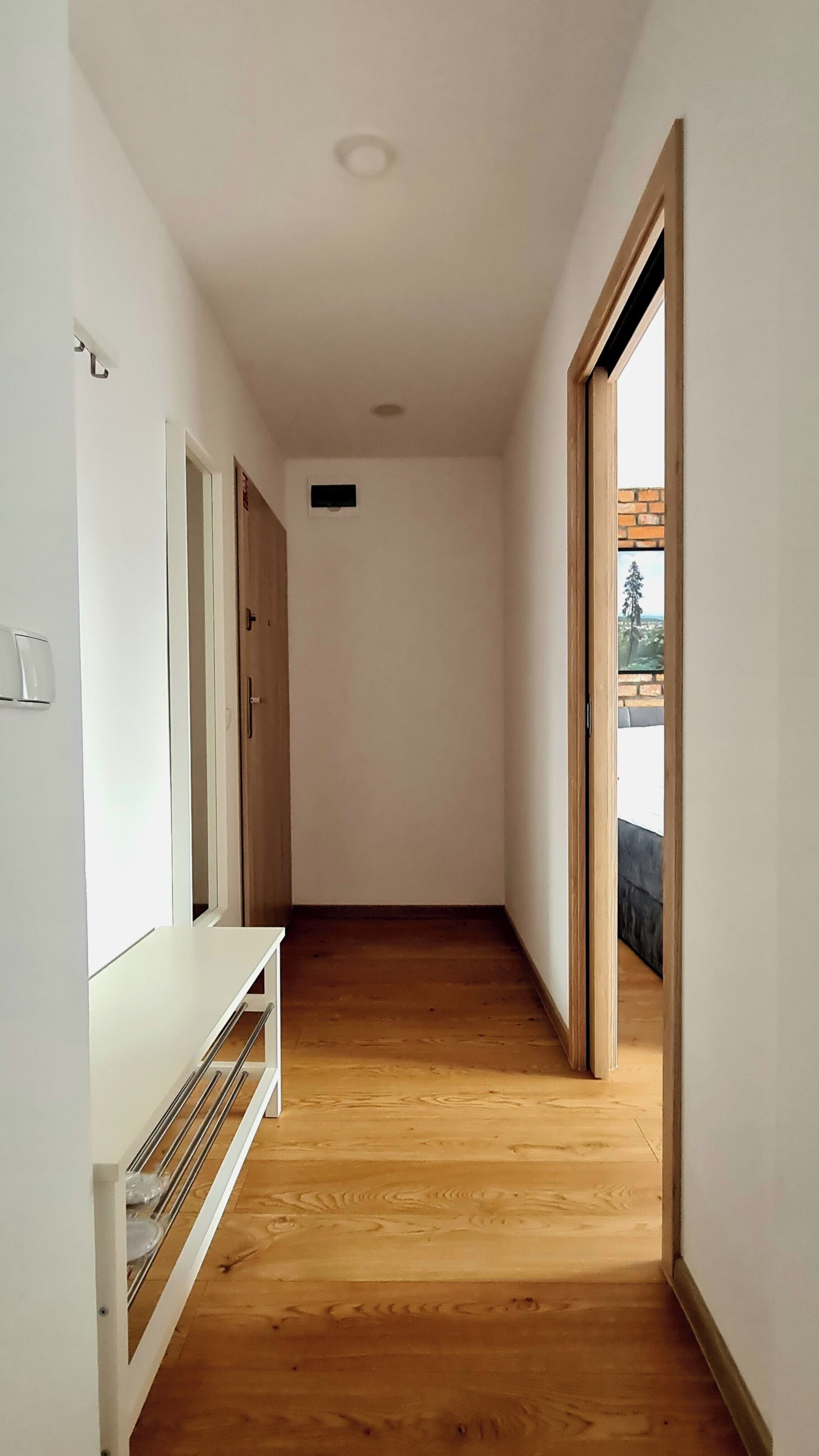 A narrow hallway with wooden flooring, white walls, and a door leading to an outdoor area.