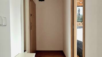 A narrow hallway with wooden flooring, white walls, and a door leading to an outdoor area.