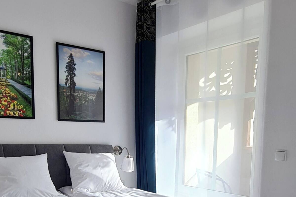 Un dormitorio moderno con una cama grande, una mesita de noche, una lámpara de pared y dos cuadros enmarcados.