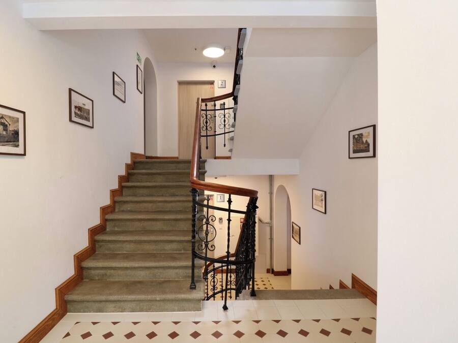 A staircase with a wooden handrail and a black metal railing, leading to an upper floor.