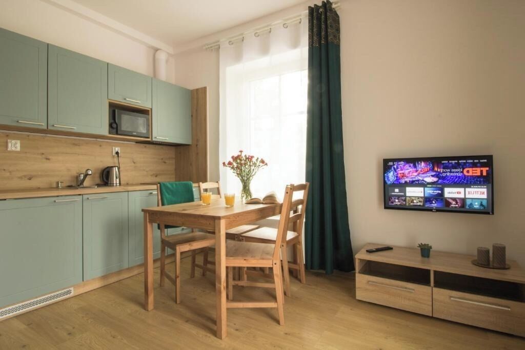 A compact kitchen with teal cabinets, a wooden dining table, and a TV mounted on the wall.