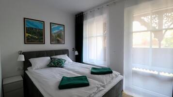 Une chambre avec un grand lit, deux tableaux encadrés au mur, une table de chevet et une fenêtre donnant sur un beau paysage.