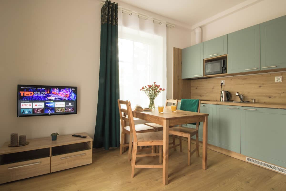 Una cocina moderna con armarios color turquesa, una mesa de comedor de madera y un televisor de pantalla plana mostrando la interfaz de un servicio de streaming.