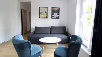 Una sala moderna con un sofá gris, dos sillones azules, una mesita blanca y dos cuadros enmarcados en la pared.