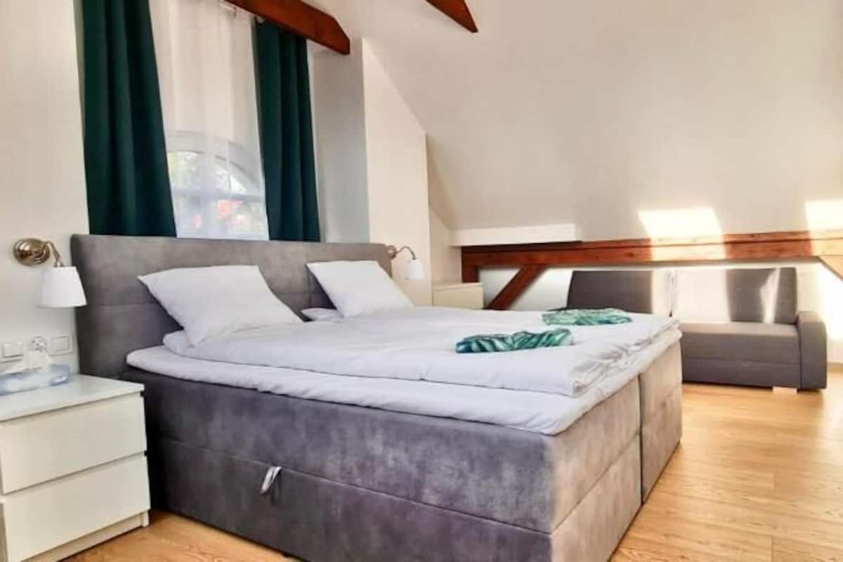Un dormitorio con cama, mesitas de noche, una silla y televisor montado en la pared.