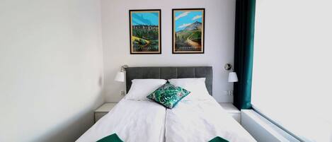A hotel room with a bed, two framed pictures on the wall, a window with curtains, and a bedside lamp.