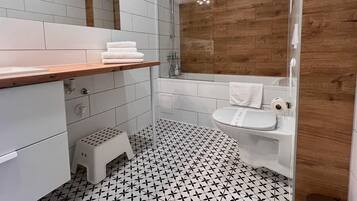 A modern bathroom with white tiles, a wooden vanity, a sink, and a shower.