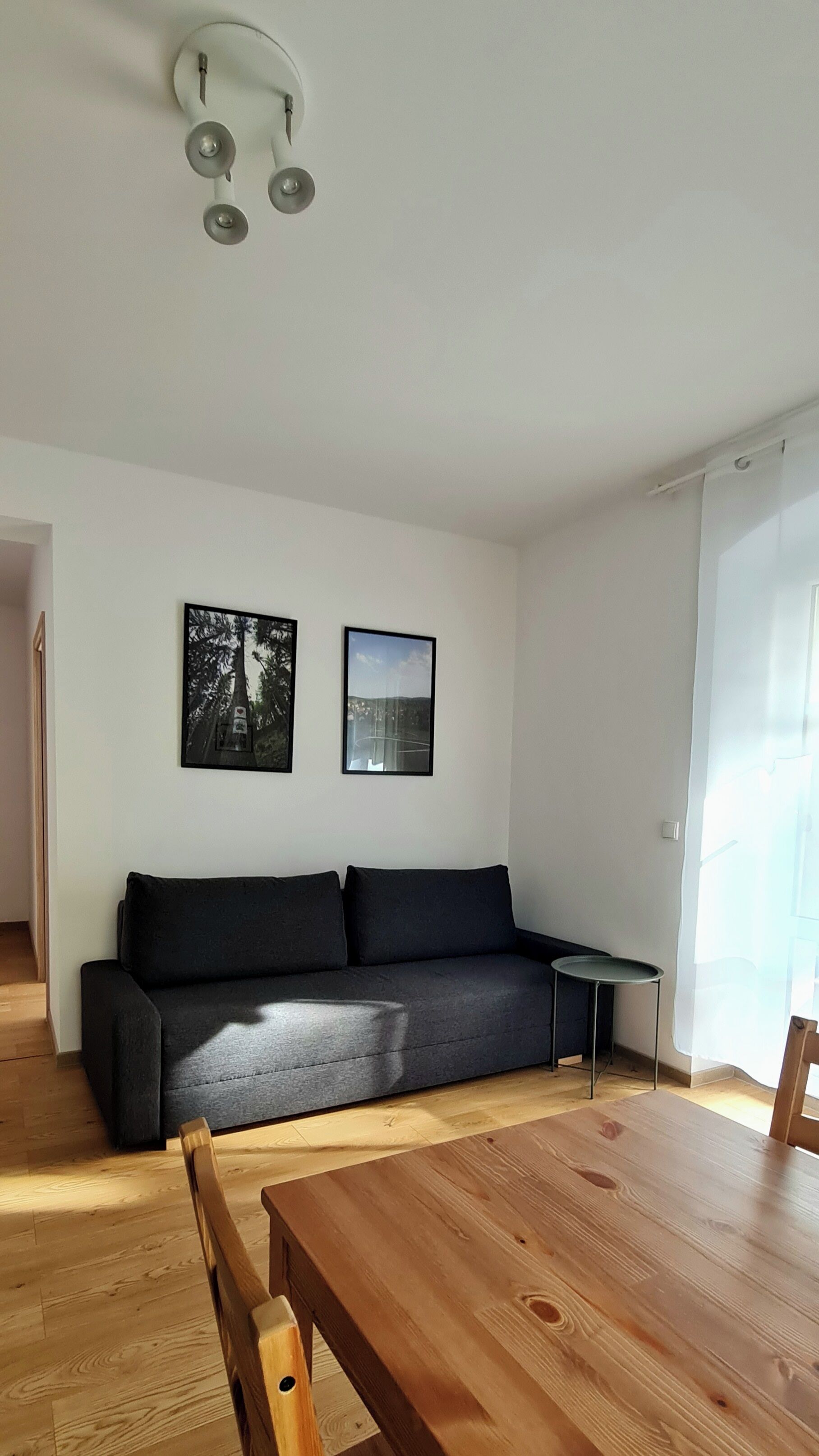 Ein modernes Wohnzimmer mit einer schwarzen Couch, einem Holzesstisch und zwei gerahmten Bildern an der Wand.