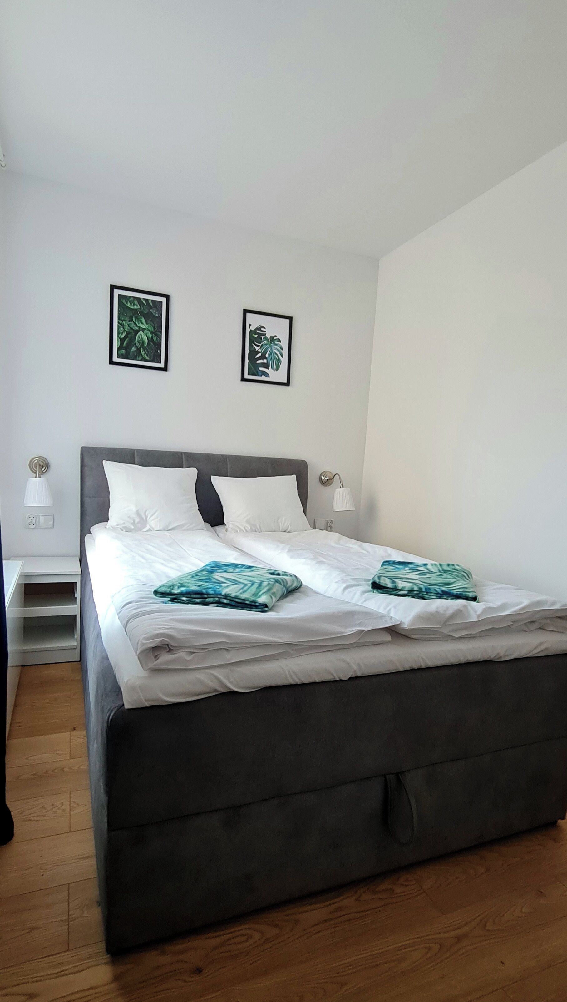 A modern bedroom with a large bed, white bedding, and two framed botanical prints on the wall.