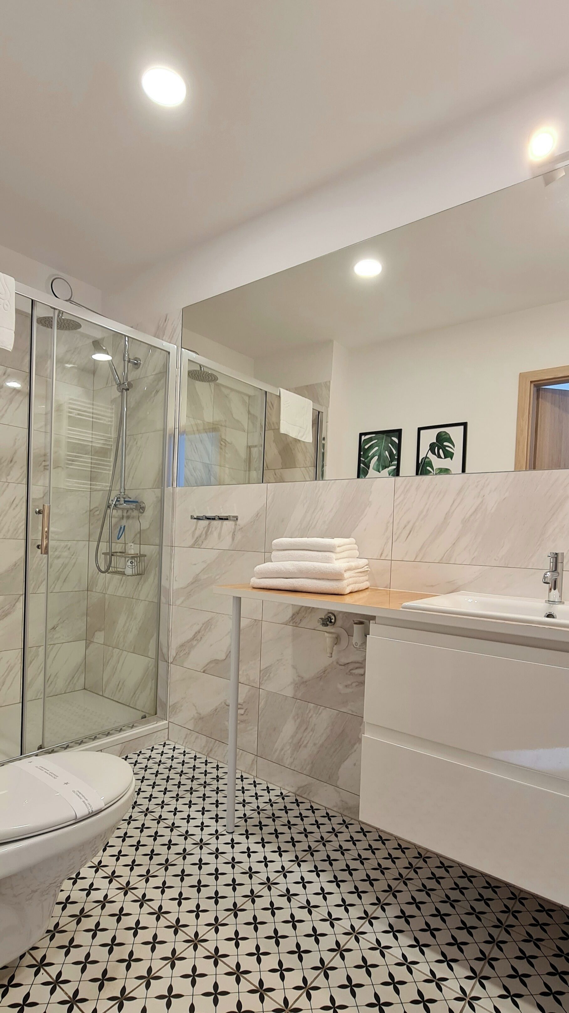 A modern bathroom with a glass-enclosed shower, a toilet, and a sink with a marble countertop.