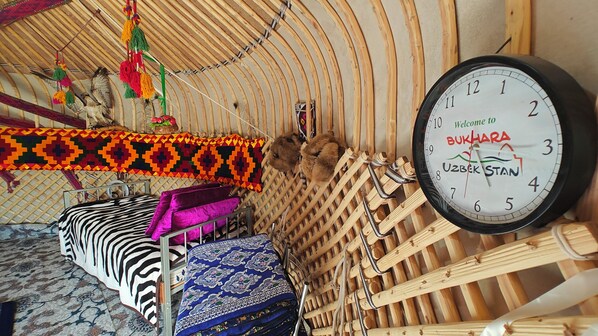 Una habitación con techo de madera curvado, un reloj, cama con ropa de cama estampada y una cesta tejida.