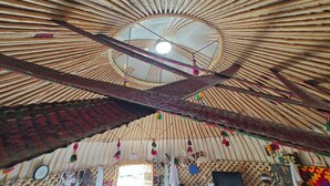 Interior de una yurtas tradicional, con techo de madera circular, soga colgante en el centro y varios objetos suspendidos.