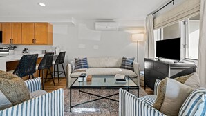A modern living room with a sofa, coffee table, and striped chairs. There is a kitchen area with wooden cabinets and a dining set. A flat-screen TV is mounted on the wall. - New Listing! Executive Rental - Steps to Vibrant Pearl Street Mall (Boulder)