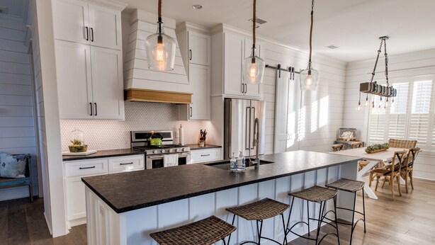 Un'ampia cucina con mobili bianchi, una grande isola con sgabelli da bar e illuminazione a sospensione.