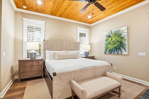 A bedroom with a wooden ceiling, a bed with a headboard, a bench, two nightstands, and a window with blinds. - Pool & Hot tub • 3-Min Walk to Beach Stylish St. Simons Cottage (St Simons)