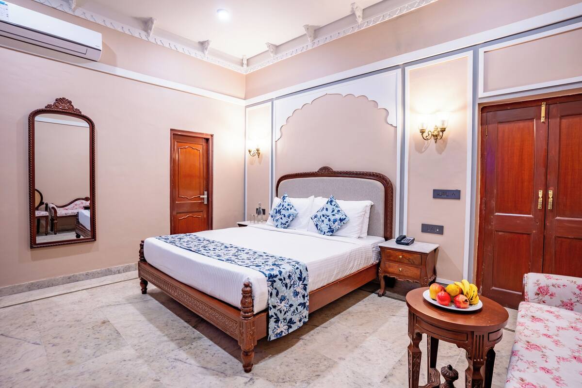 Un dormitorio con una cama de madera, una mesita de noche, una mesa redonda con fruta, una silla, un espejo y un armario.