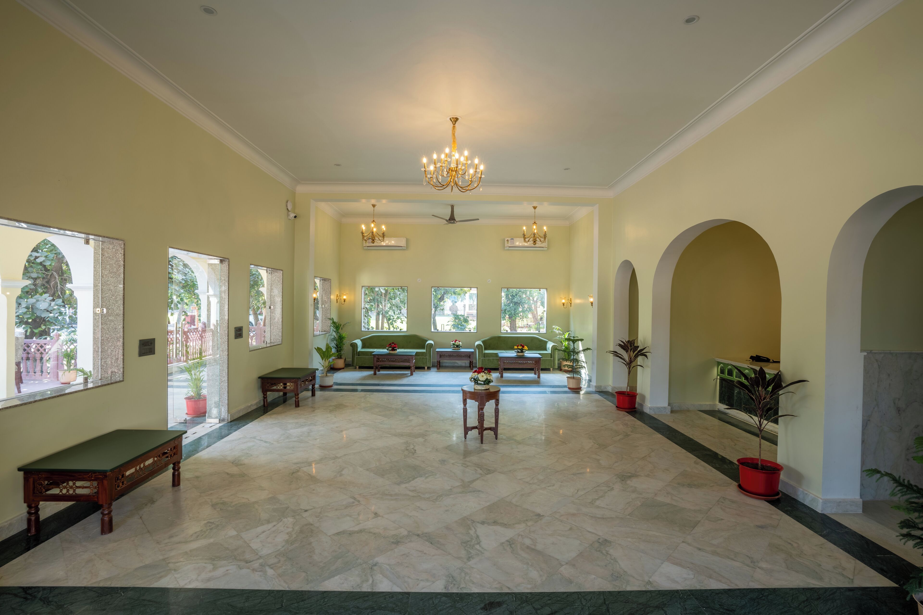 A spacious lobby with a high ceiling, chandeliers, and green sofas.