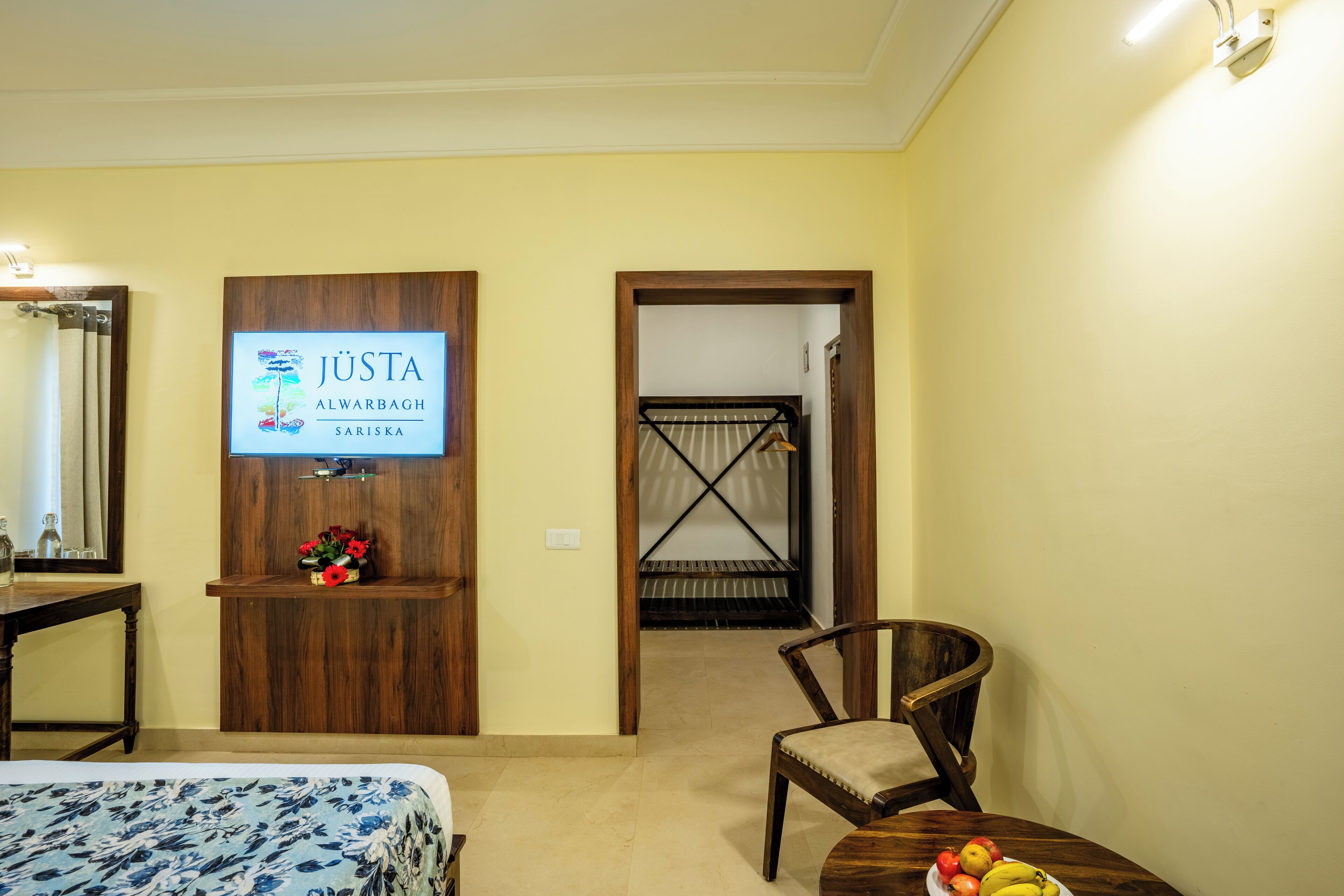 A hotel room with a bed, a wooden desk, a chair, a table with fruit, and a sign on the wall.