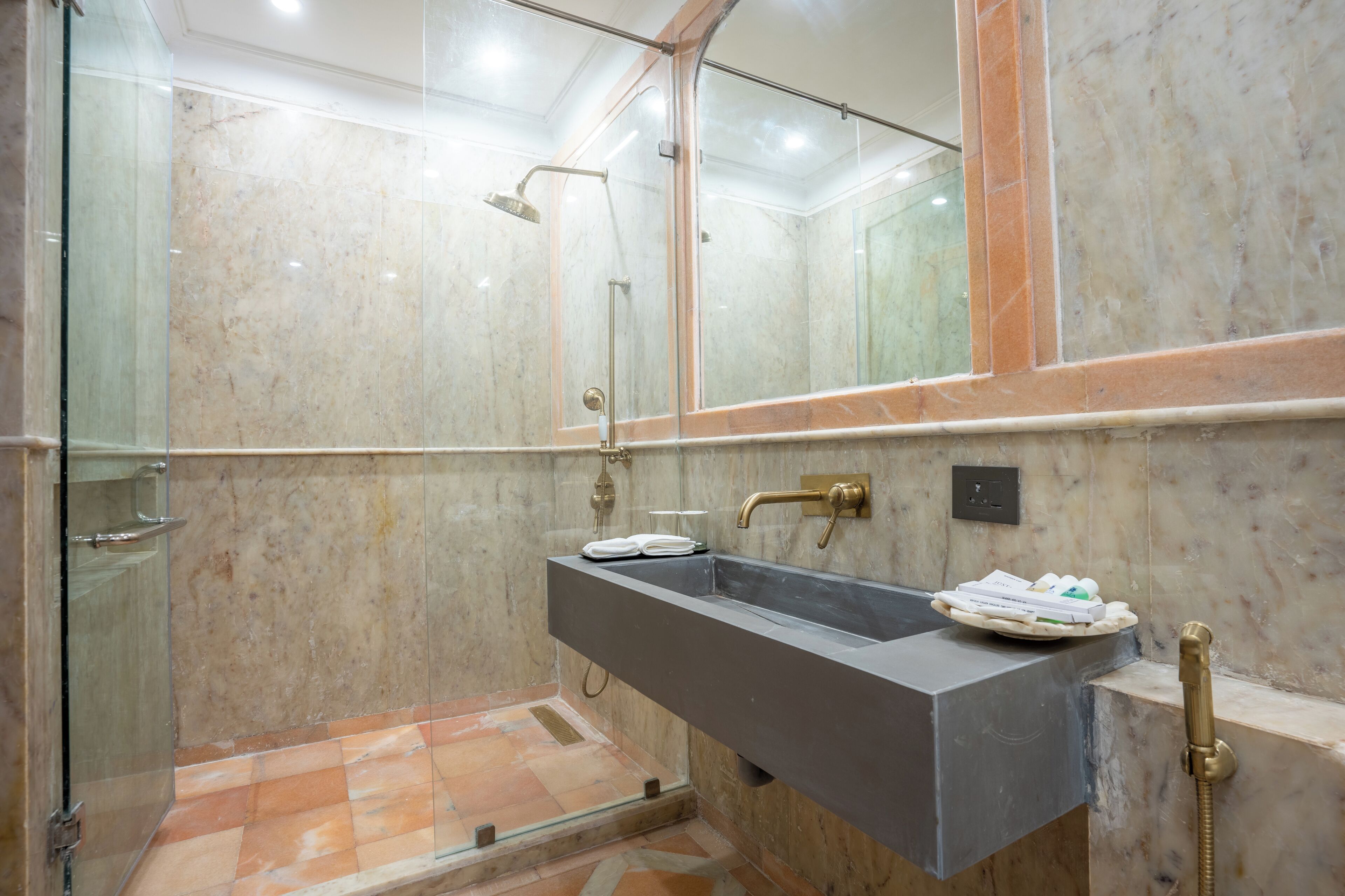 A modern bathroom with a glass-enclosed shower, a marble-tiled floor, and a built-in sink with a towel rack.