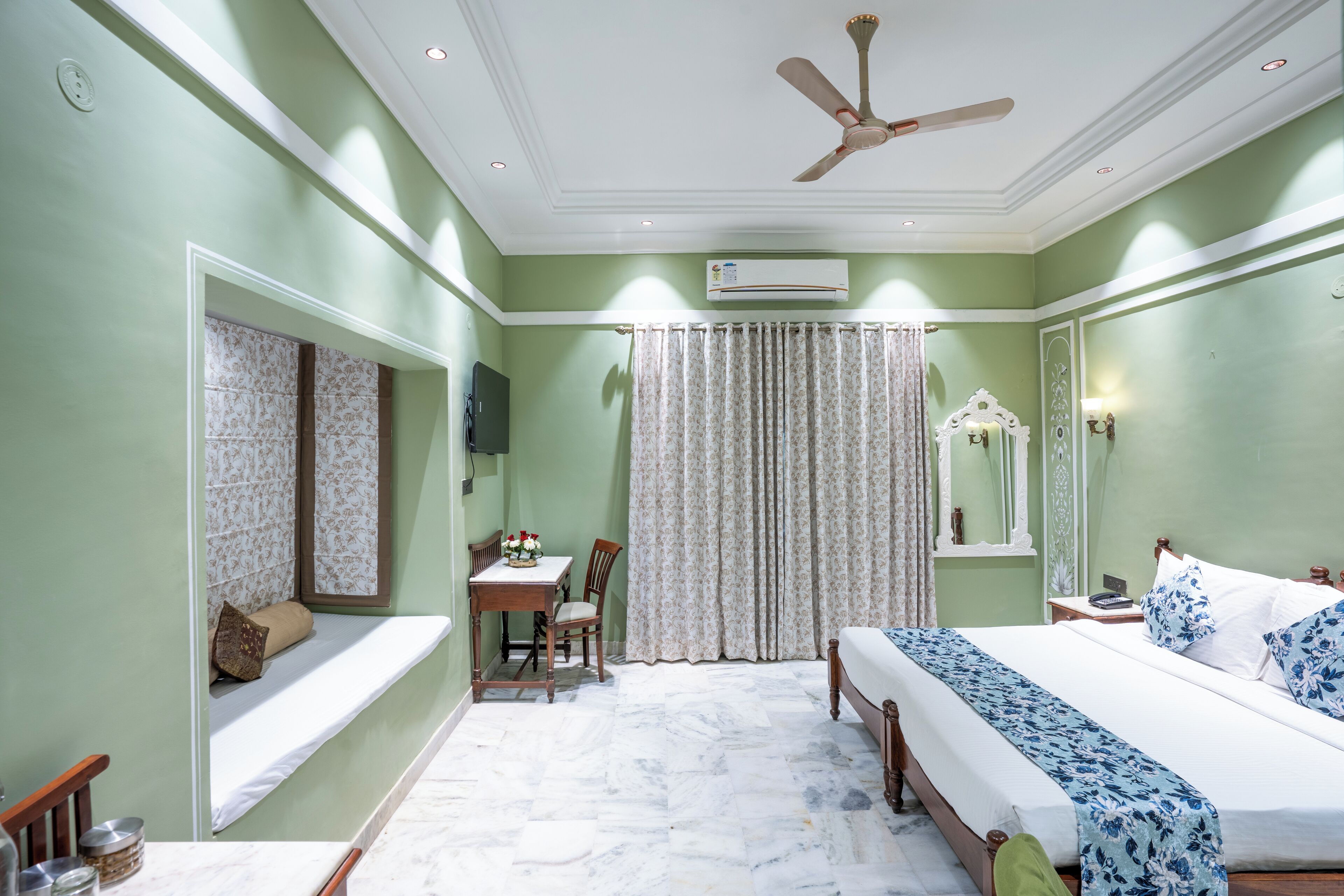 A bedroom with a bed, a desk, a chair, a window seat, and a ceiling fan.