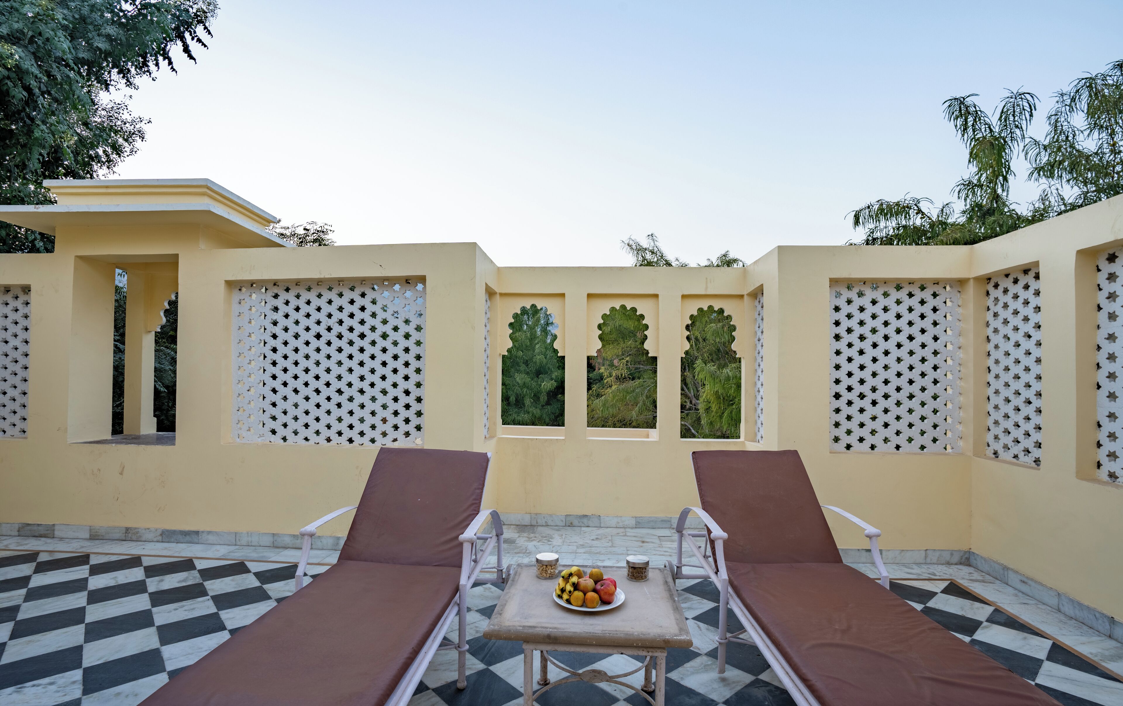 A sunlit outdoor seating area with two lounge chairs and a table with fruit.