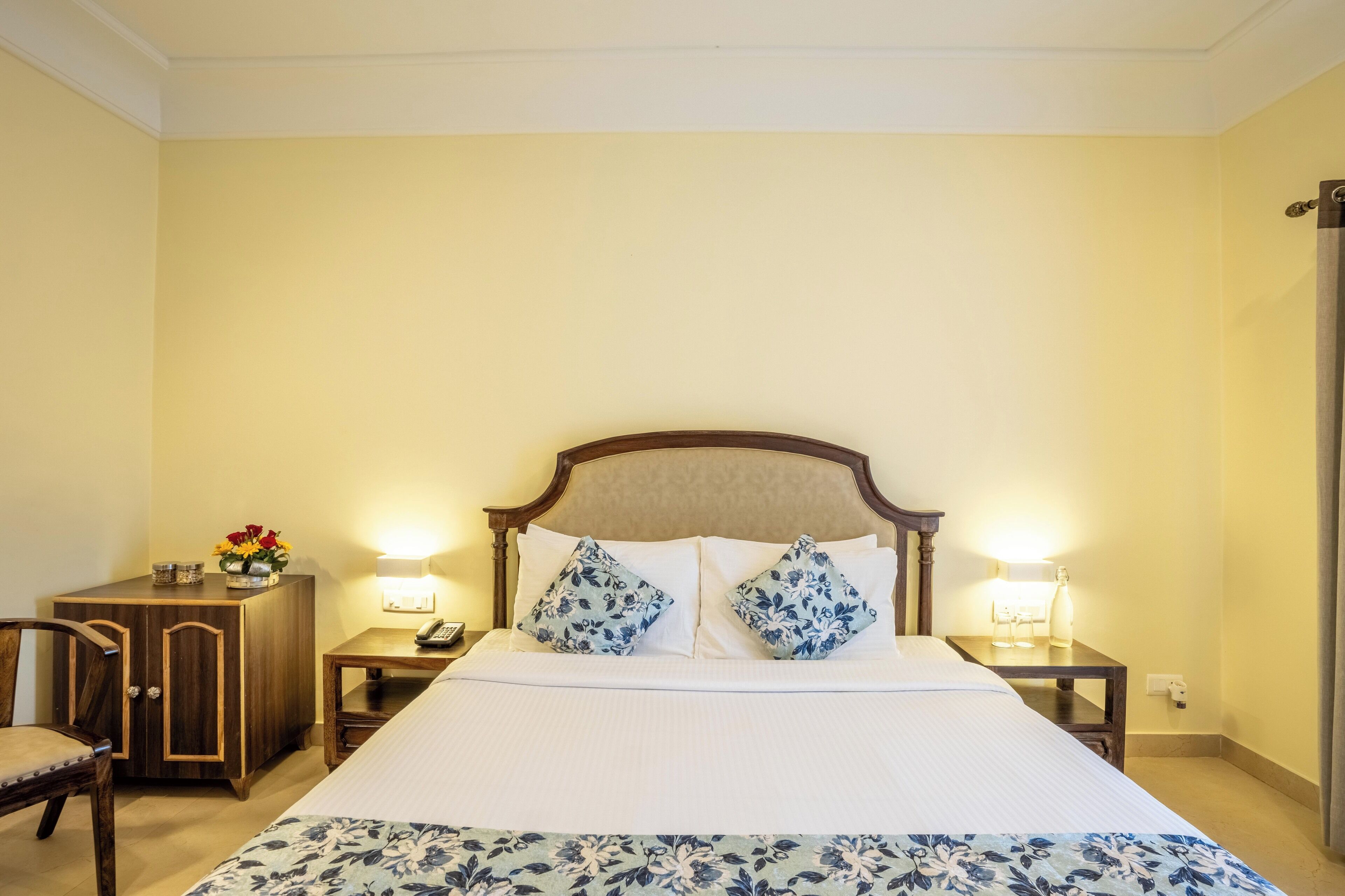 A neatly arranged hotel room with a large bed, two bedside tables with lamps, a wooden nightstand, a small cabinet, and a chair.