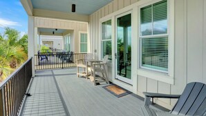 A covered porch with a table and chairs, a bench, and a door with glass panels. - West Side Cottages B by Liquid Life (Gulf Shores)
