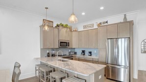 A modern kitchen with a central island, stainless steel appliances, and light wood cabinetry. - West Side Cottages B by Liquid Life (Gulf Shores)