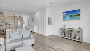 A modern living room with a grey sofa, wooden flooring, a white console table, and a painting of a beach scene. - West Side Cottages B by Liquid Life (Gulf Shores)
