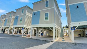 A row of modern, multi-story buildings with covered parking areas and a clear blue sky. - West Side Cottages B by Liquid Life (Gulf Shores)
