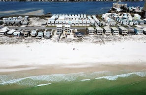 Vista aérea de una zona costera con varios edificios frente a la playa, una playa de arena y una masa de agua.
