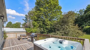 A hot tub on a wooden deck with a picnic table and grill, surrounded by trees. - Serene 4-BR Farmhouse 5 min to Okemo (Ludlow)