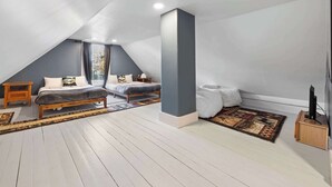 A modern loft bedroom with a sloped ceiling, a large bed, a TV stand, and a window with curtains. - Serene 4-BR Farmhouse 5 min to Okemo (Ludlow)