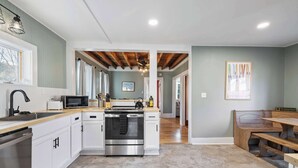 A modern kitchen with white cabinets, stainless steel appliances, and a wooden countertop. There is a dining area with a bench and a table. - Serene 4-BR Farmhouse 5 min to Okemo (Ludlow)