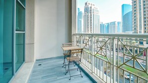 Een balkon met een tafel en stoelen, uitzicht op hoge gebouwen, en een hekwerk.