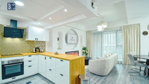 Een moderne keuken met witte kasten, een houten aanrechtblad en een ingebouwde oven. Er is een zithoek met een witte bank en een tafel.