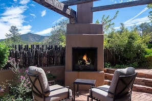 An outdoor patio with a stone fireplace, two cushioned chairs, and a wooden fence.