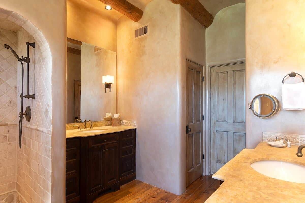 Une salle de bain dotée d’un double lavabo, de meubles en bois foncé, d’un grand miroir et d’une douche au design incurvé.