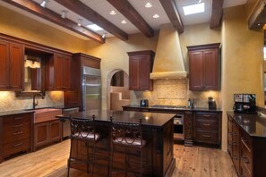 Una cucina moderna con mobili in legno, un'isola grande con sgabelli da bar, un forno integrato e un frigorifero in acciaio inossidabile.