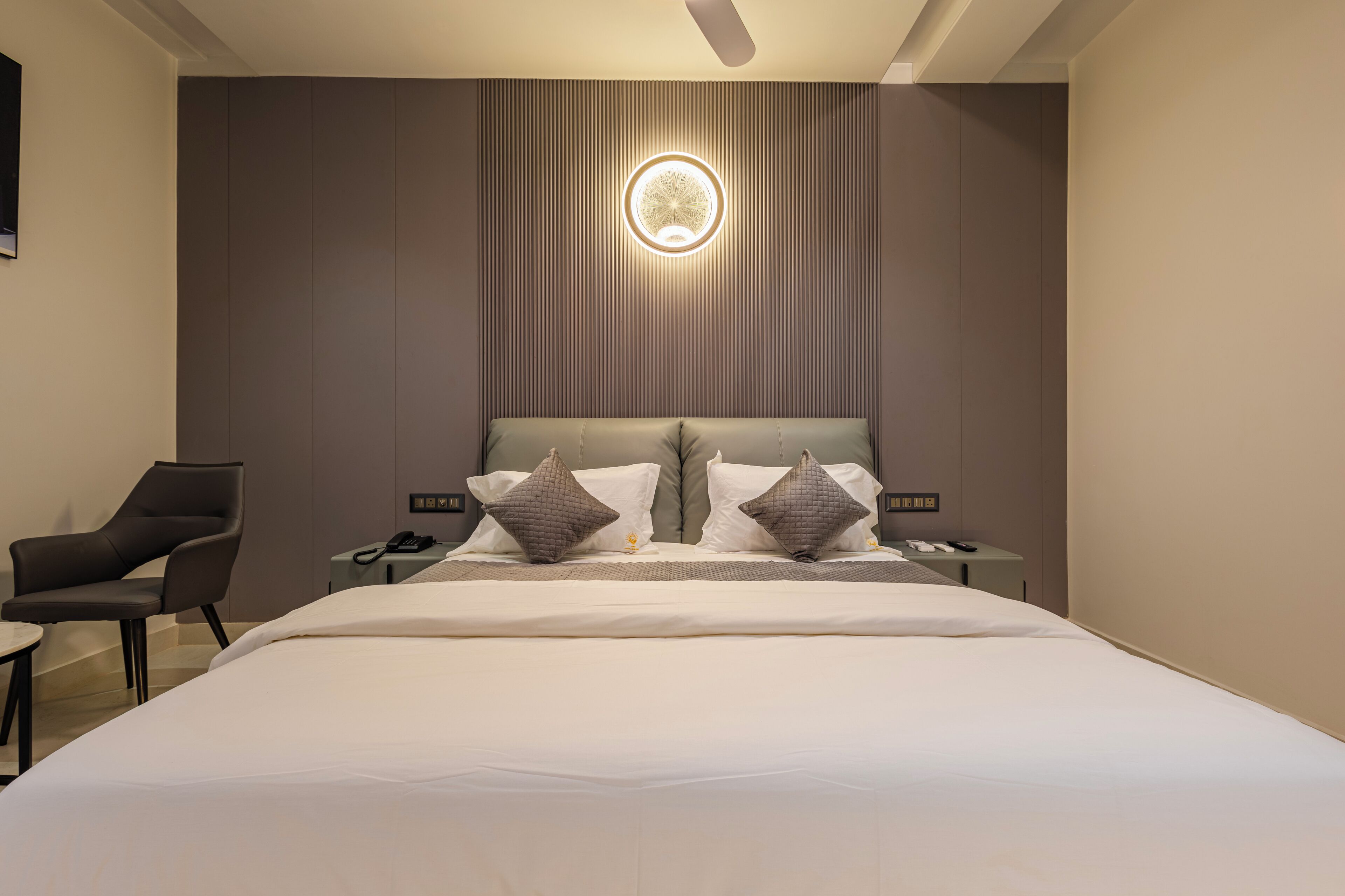 Una habitación de hotel moderna con una cama grande, una silla, una mesita de noche y un aplique de pared.