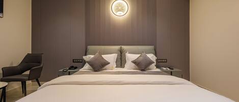 Una habitación de hotel moderna con una cama grande, una silla, una mesita de noche y un aplique de pared.