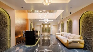 Eine geräumige Lobby mit Marmorboden, einem schwarzen Empfangstresen, einem beigen Sofa und einer Chandelier.