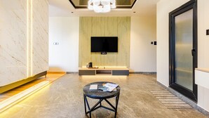 Eine moderne Hotellobby mit Marmorboden, einem runden Tisch mit Papieren, einem Flachbildfernseher an der Wand und einer großen Tür mit Glasfenster.