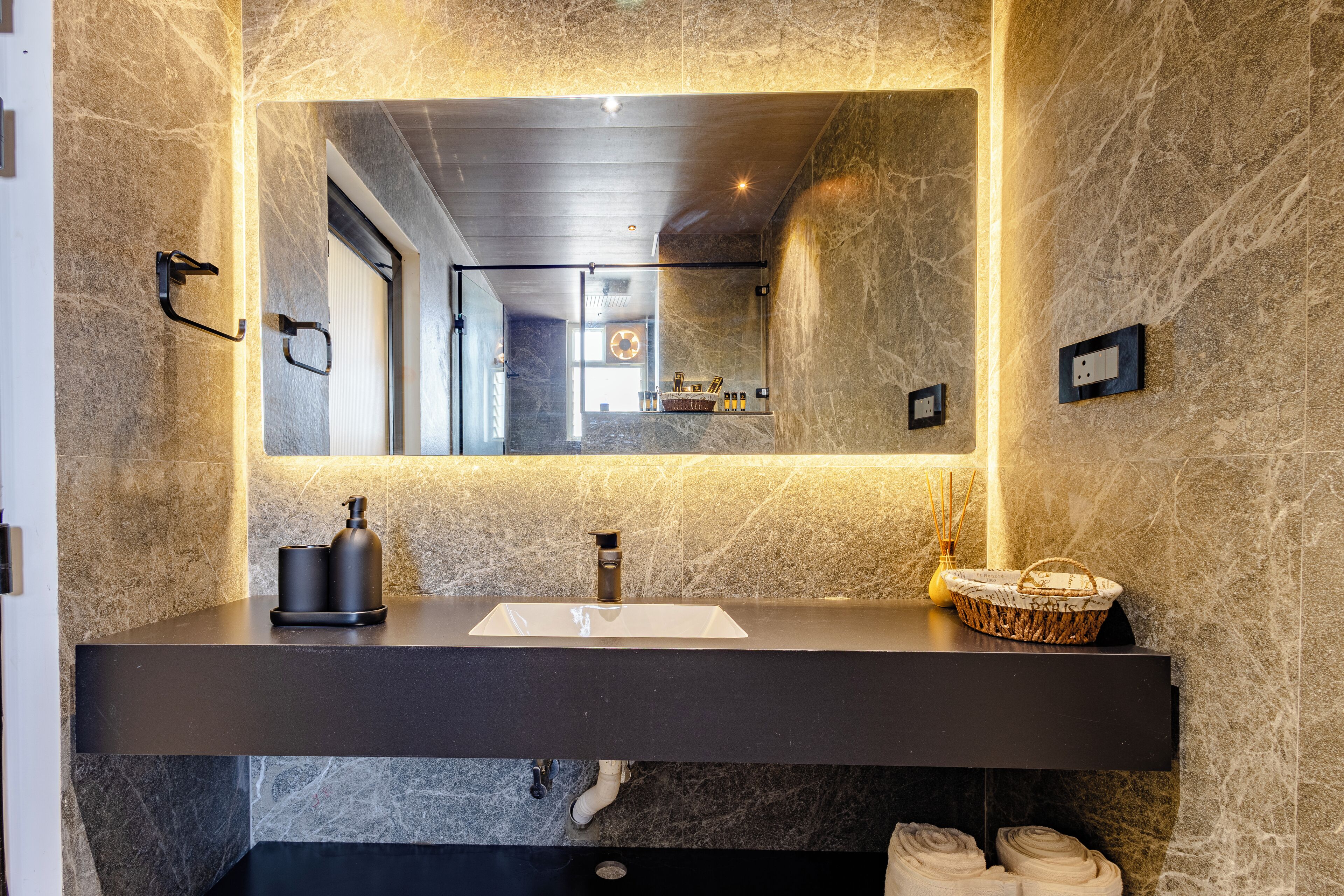 A modern bathroom with a marble sink, a large mirror, and a basket of toiletries.
