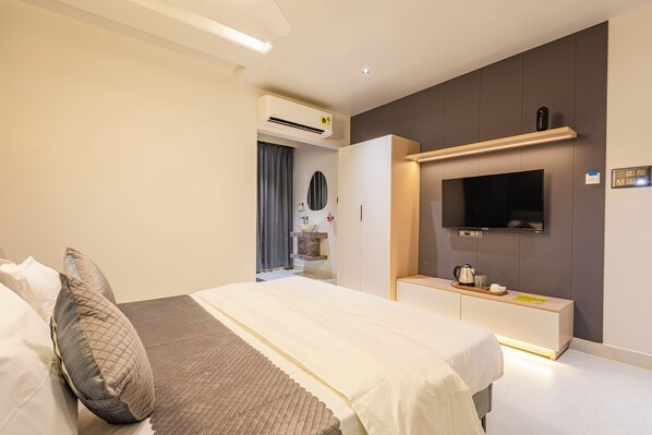 Una habitación de hotel moderna con una cama grande, un televisor montado en la pared y un escritorio integrado con cafetera.
