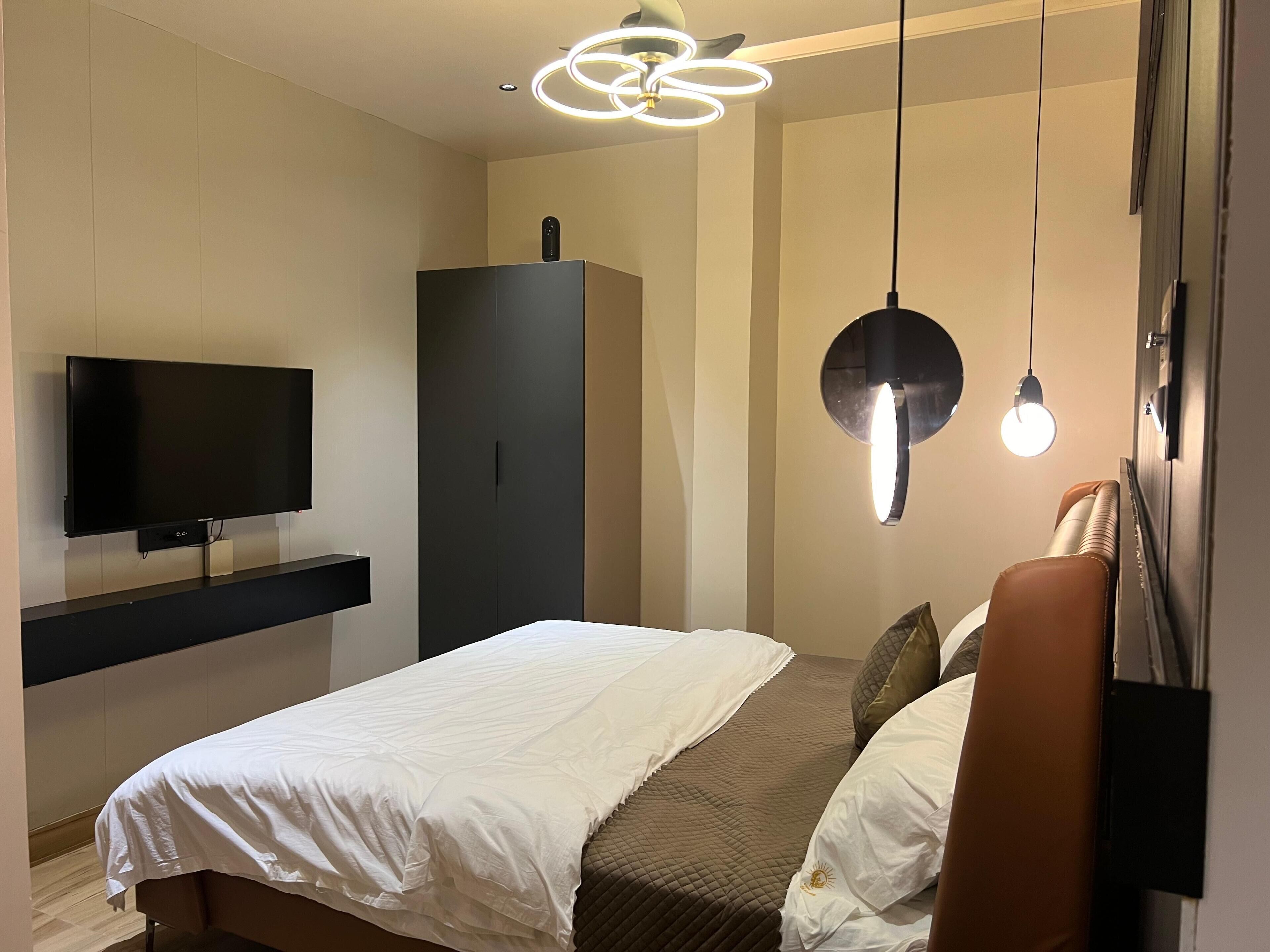 A modern bedroom with a bed, a TV, a wardrobe, and pendant lights.