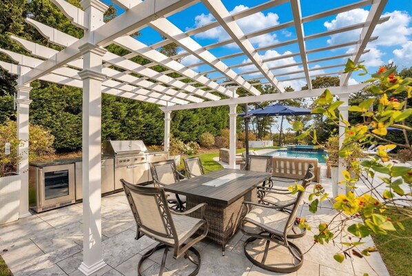 An outdoor patio with a pergola, a grill, a pool, and a table with chairs.