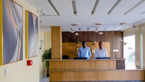 Zona de recepción con un mostrador de madera, dos empleados y un diseño de techo moderno.