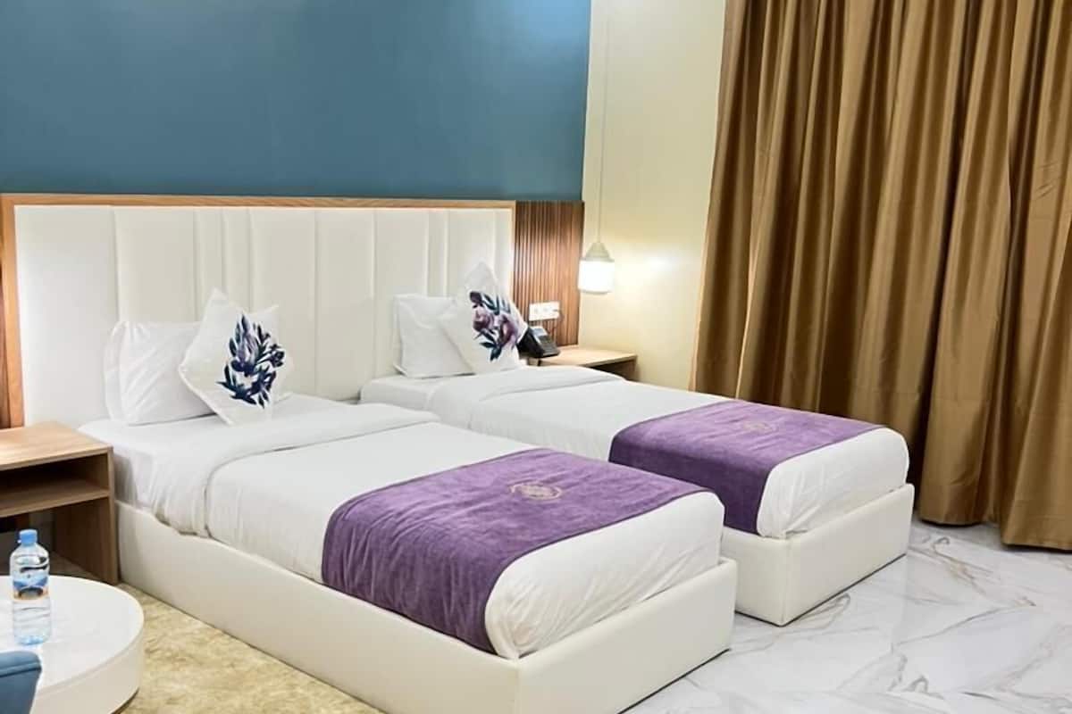 A hotel room with two beds, a round table, a nightstand, a lamp, and a large window with curtains.