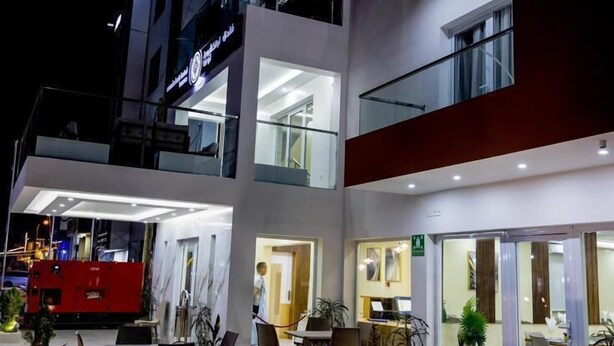 Un hotel de varios pisos con una terraza exterior bien iluminada, múltiples balcones y un restaurante o cafetería visible en la planta baja.